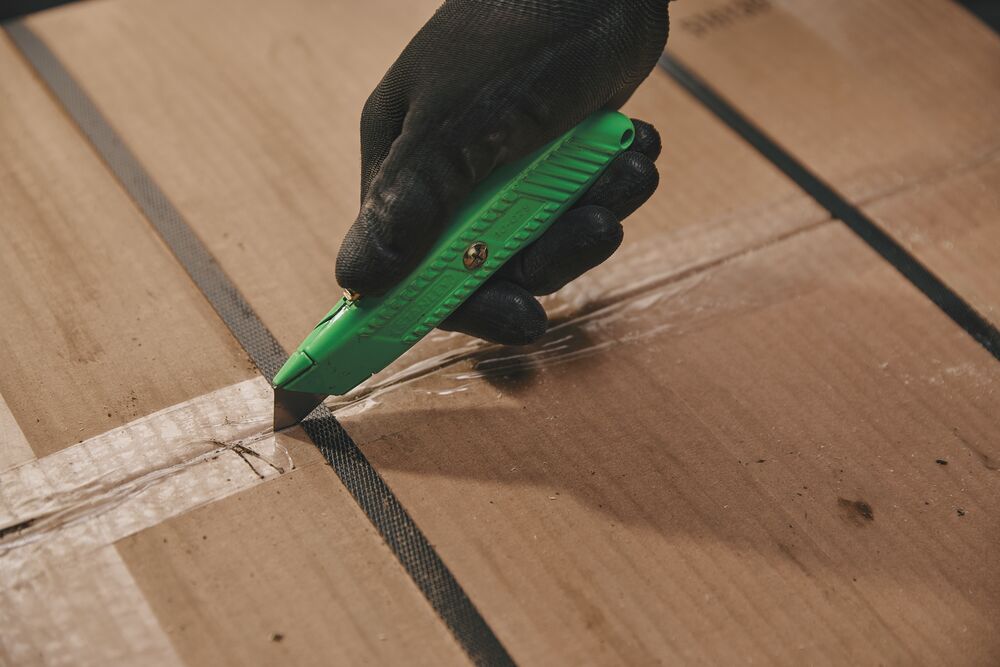 STANLEY 10-179 utility knife in green cutting packaging tape on a cardboard box close-up.