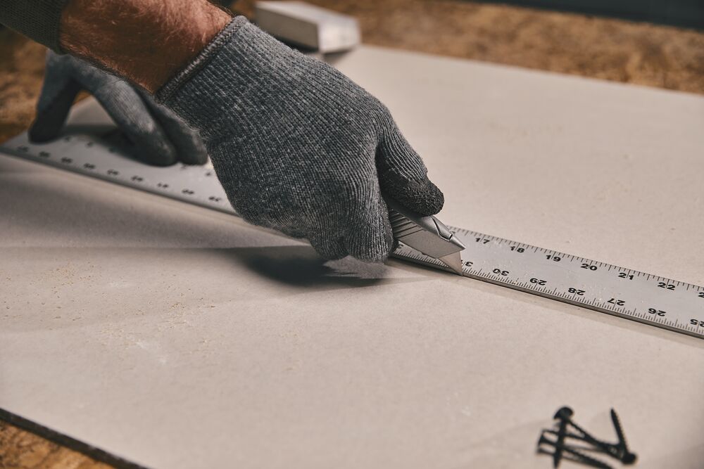 STANLEY 10-299 utility knife cutting along a metal ruler on a sheet, close-up hand with glove.
