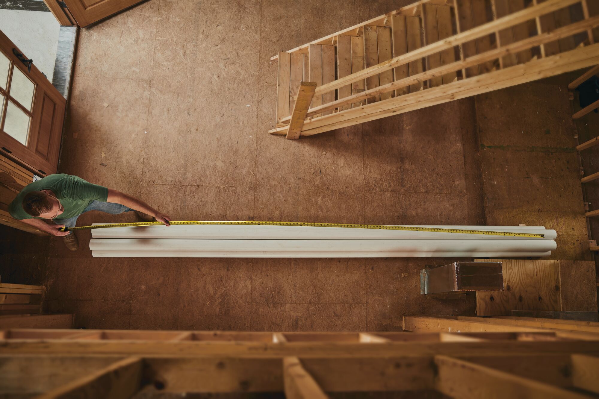 STANLEY 33-725 tape measure extended to measure long white boards in a wood workshop, top-down view.