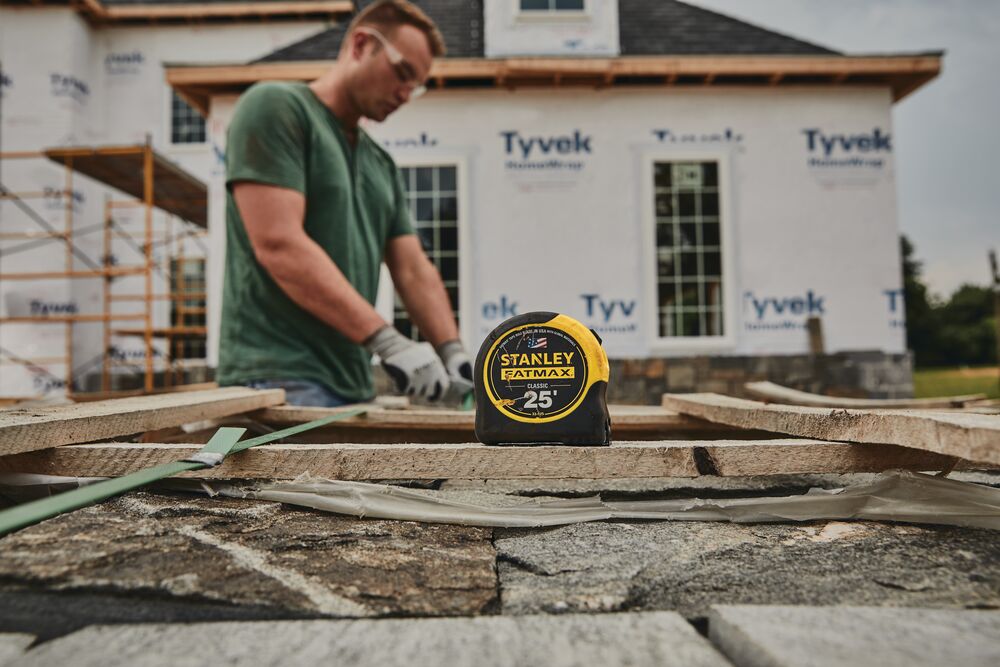 STANLEY 33-725 tape measure on stone surface at construction site, home under renovation in background.