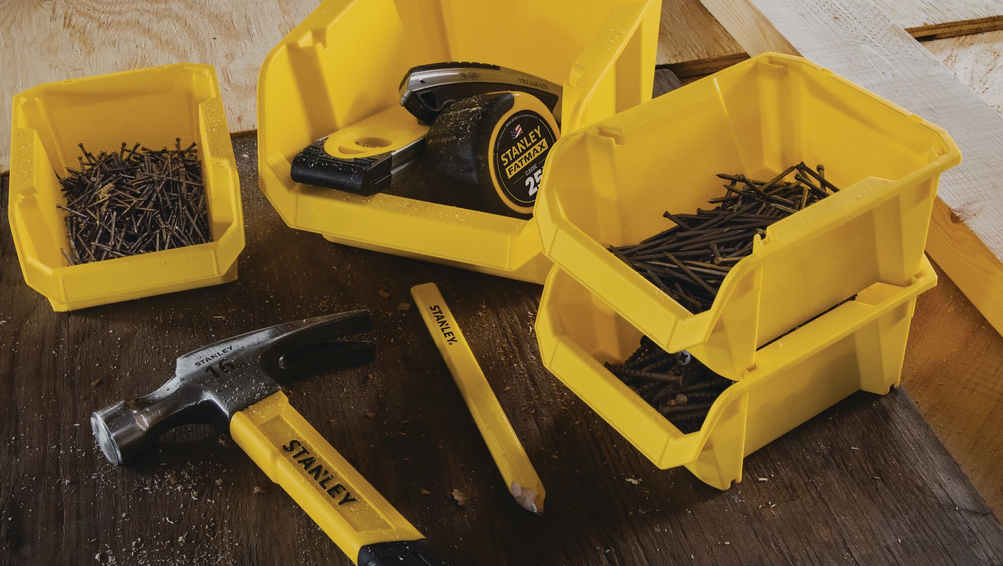 STANLEY ST yellow storage bins with nails, hammer, tape measure, and chisel on wooden surface, front view.