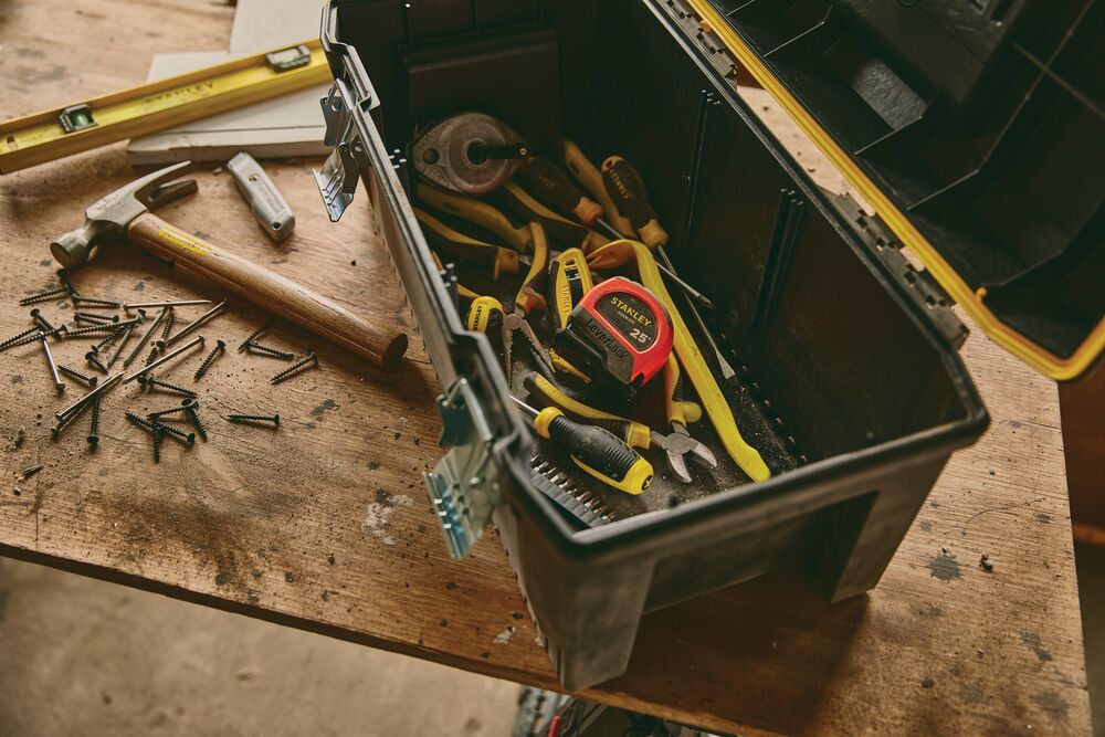 STANLEY STHT30817S tape measure in open black toolbox with assorted hand tools on wooden workbench.