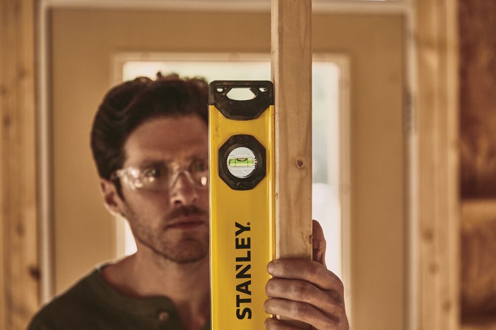STANLEY STHT42496 level tool in use, held vertically against a wooden stud in a construction setting.
